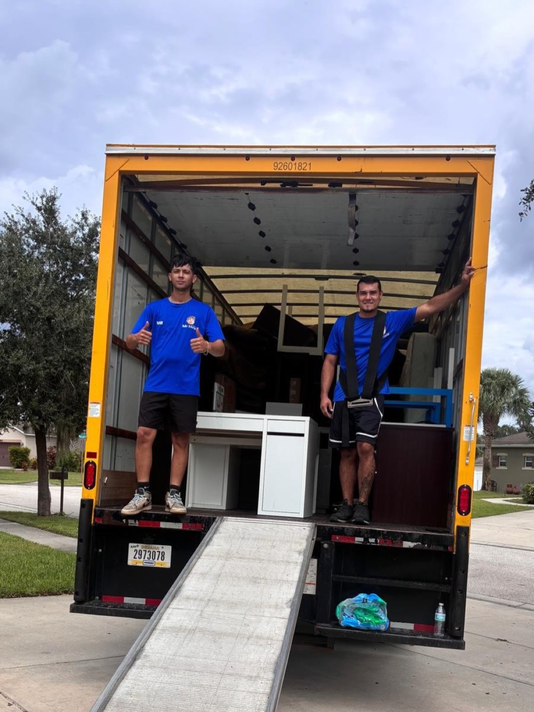 Two Solutions Mr.Help crew members in blue uniform shirts standing on the ramp of a loaded moving truck