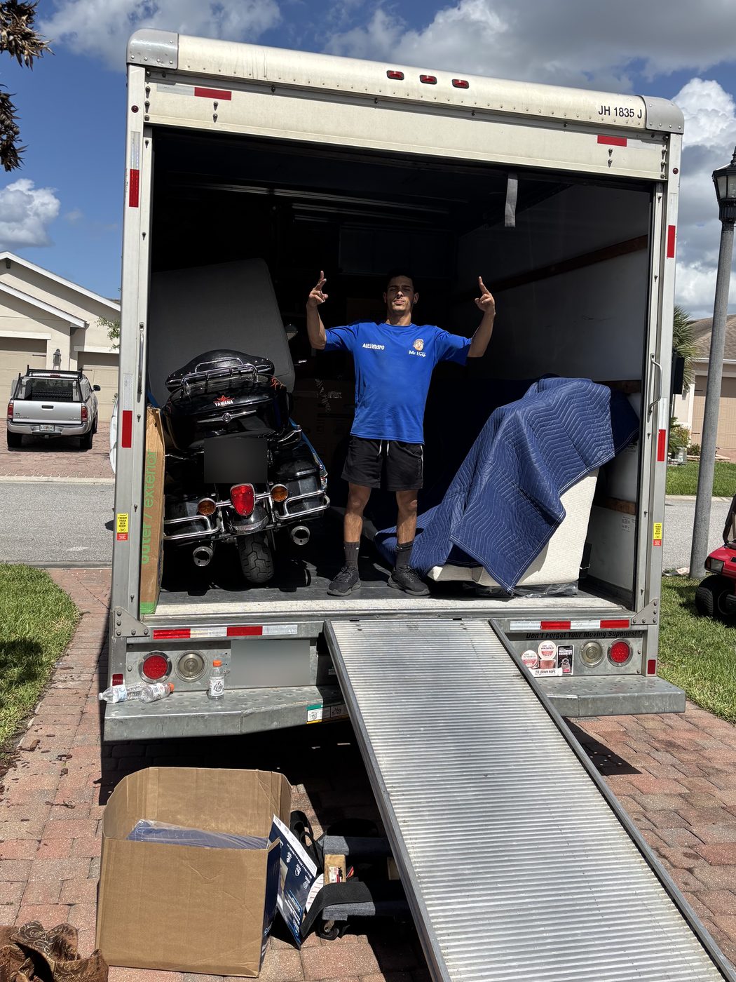 A Solutions Mr.Help crew member in a blue uniform shirt inside a loaded moving truck, with a motorcycle strapped in and furniture wrapped in moving blankets
