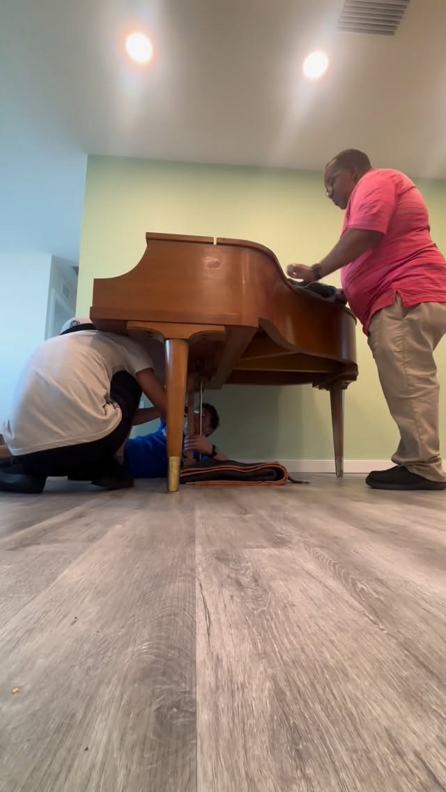 Crew wrapping and lifting a baby grand piano inside a home
